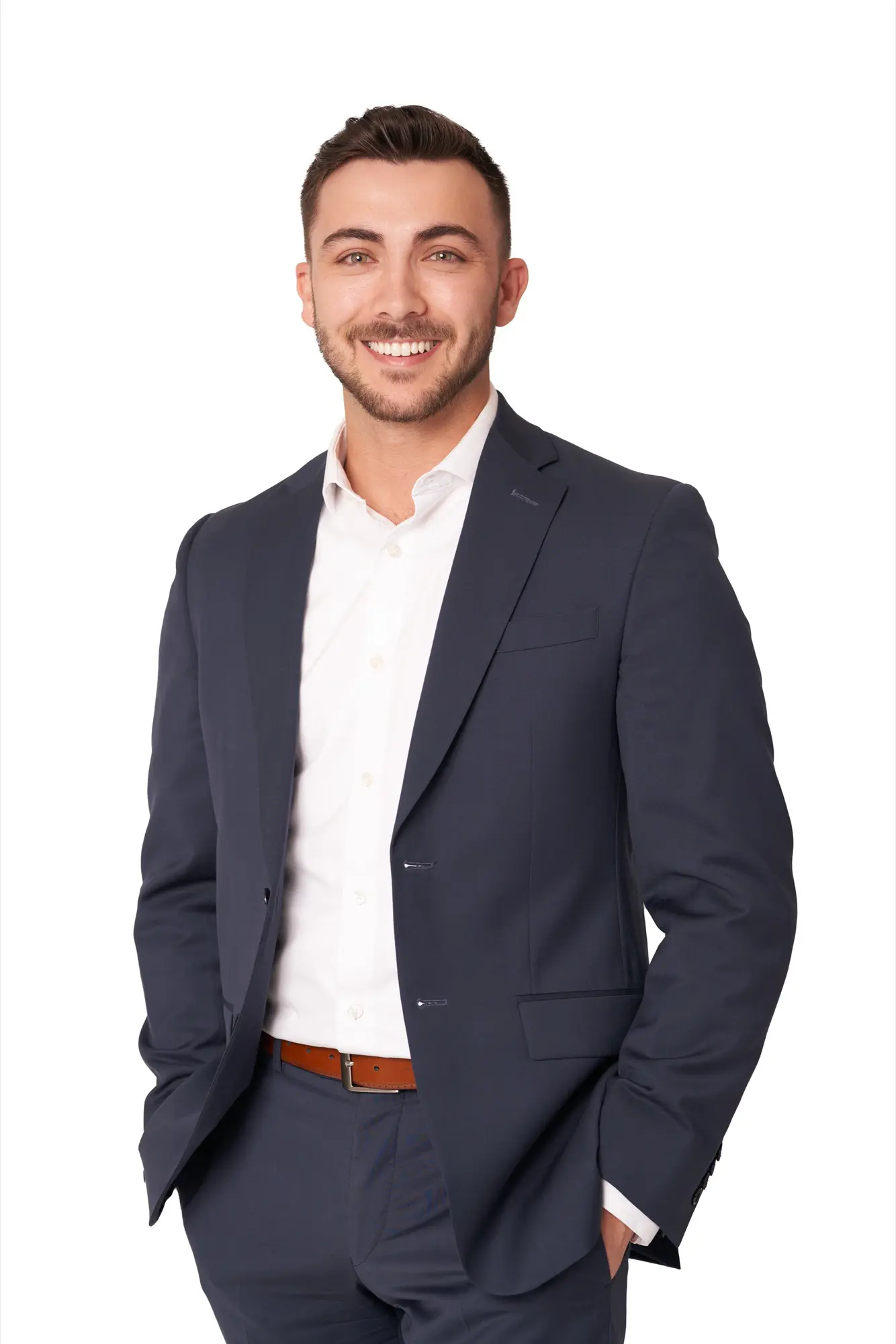 Man in a navy suit with hands in pockets in a professional headshot on a white studio background in Kelowna