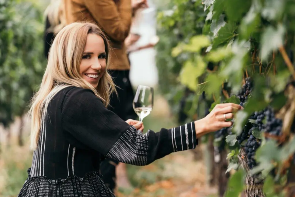 Woman holding a wine glass while picking grapes in a vineyard
