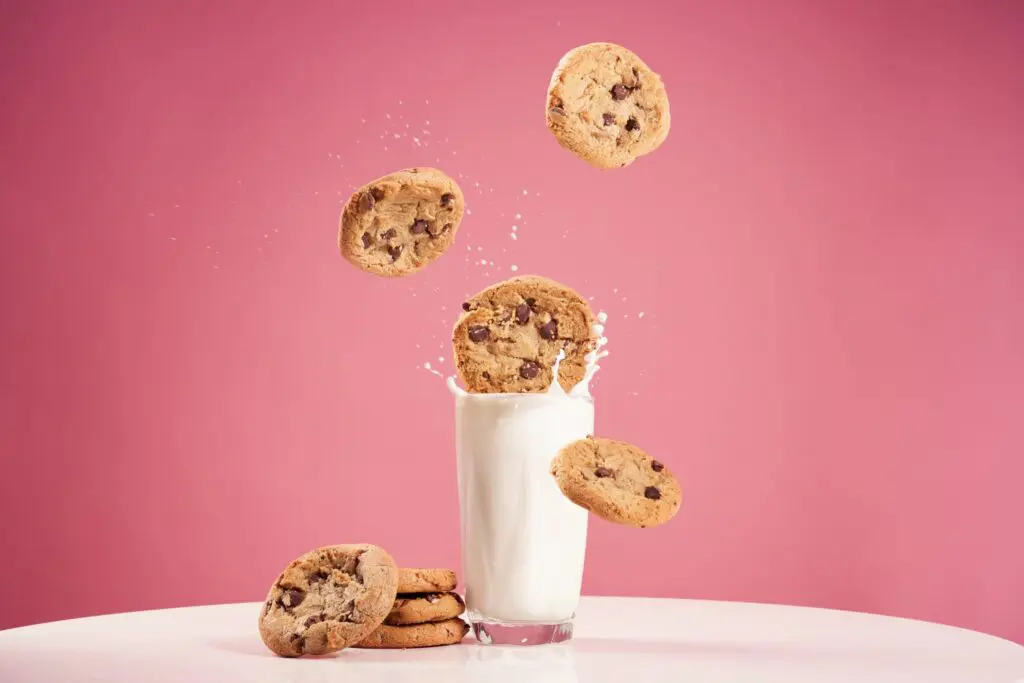 Cookies splashing into a glass of milk against a pink backdrop