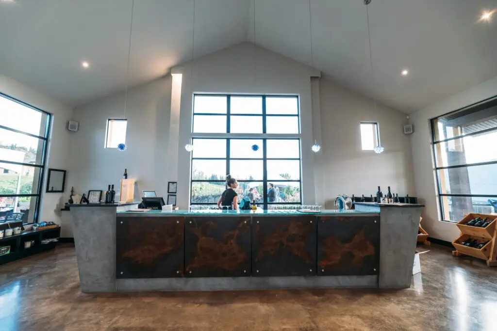 Winery tasting bar with a concrete counter and tall windows looking out to the vineyard